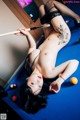 A naked woman laying on a pool table holding a cue.