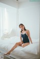 A woman sitting on a bed in a blue swimsuit.