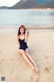 A woman in a black bathing suit sitting on a beach.