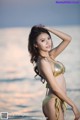 A woman in a gold bikini standing on the beach.