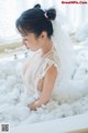 A woman in a white dress sitting in a bathtub filled with foam.