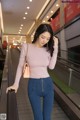 A woman in a pink top and blue jeans is walking down an escalator.