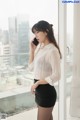 A woman in a white shirt and black skirt talking on a cell phone.