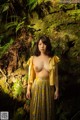 A woman in a yellow shirt and skirt standing in a forest.