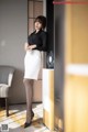 A woman in a black shirt and white skirt leaning against a wall.