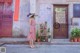 A woman in a pink dress and hat standing in front of a building.