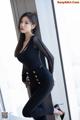 A woman in a black bodysuit leaning against a window.