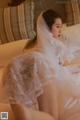 A woman in a wedding dress sitting on a bed.