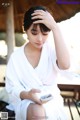 A woman in a white robe sitting on a bench looking at her phone.