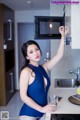 A woman in a blue bathing suit standing in front of a microwave.