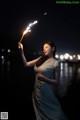 A woman holding a sparkler in her hand at night.