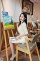 A woman sitting in front of a painting on a easel.