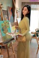 A woman in a yellow dress is painting on a easel.