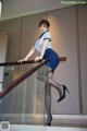 A woman in a blue dress and black stockings is standing on a railing.