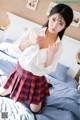 A woman in a white shirt and red plaid skirt posing on a bed.