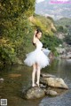 A woman in a white dress standing on a rock in the water.