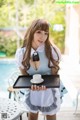 A woman in a maid outfit holding a tray with a cup of coffee.