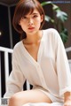 A woman sitting on top of a bed wearing a white shirt.