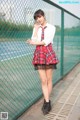 A woman in a school uniform standing next to a fence.