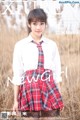 A young woman in a school uniform standing in a field.