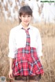 A young woman in a school uniform standing in a field.