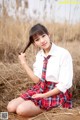 A young woman in a school uniform sitting in a field.