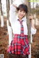 A young woman in a school uniform leaning against a tree.