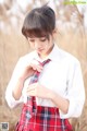 A woman in a white shirt and red plaid skirt adjusting her tie.