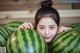 A young woman holding a large watermelon in front of her face.