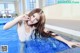 A woman in a white tank top sitting in a swimming pool.