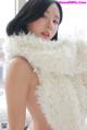 A woman in a white fur coat posing on a bed.