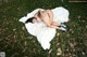 A woman laying on a white rug in the grass.