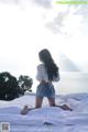 A woman sitting on top of a bed next to the ocean.