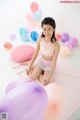 A young girl sitting on the floor surrounded by balloons.