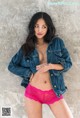 A woman in a denim jacket and pink panties posing for a picture.