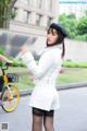 A woman in a white jacket and black hat standing next to a bike.