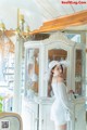 A woman in a white dress and hat standing in front of a cabinet.