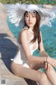 A woman in a white bathing suit and hat sitting by a pool.