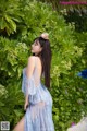 A woman in a blue dress standing in front of a bush.