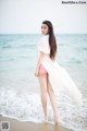 A woman in a white shirt and pink panties standing on the beach.