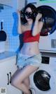 A woman in a red top and denim shorts posing in front of a washing machine.